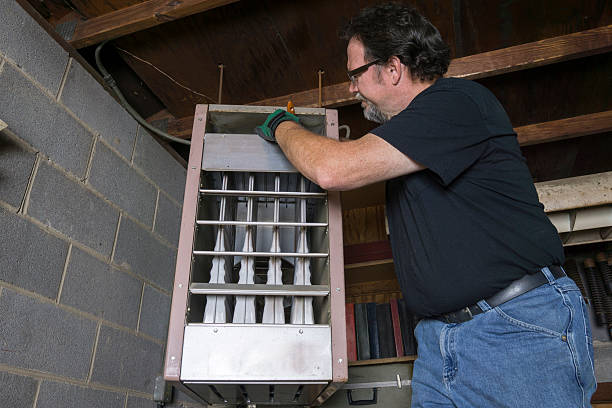 Repairman cleaning the upper duct of a overhead gas heater.
